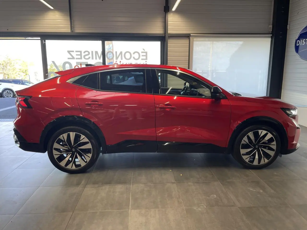 Profil côté gauche du Renault Rafale 2025 rouge avec toit noir et jantes alliage diamantées noires en showroom.