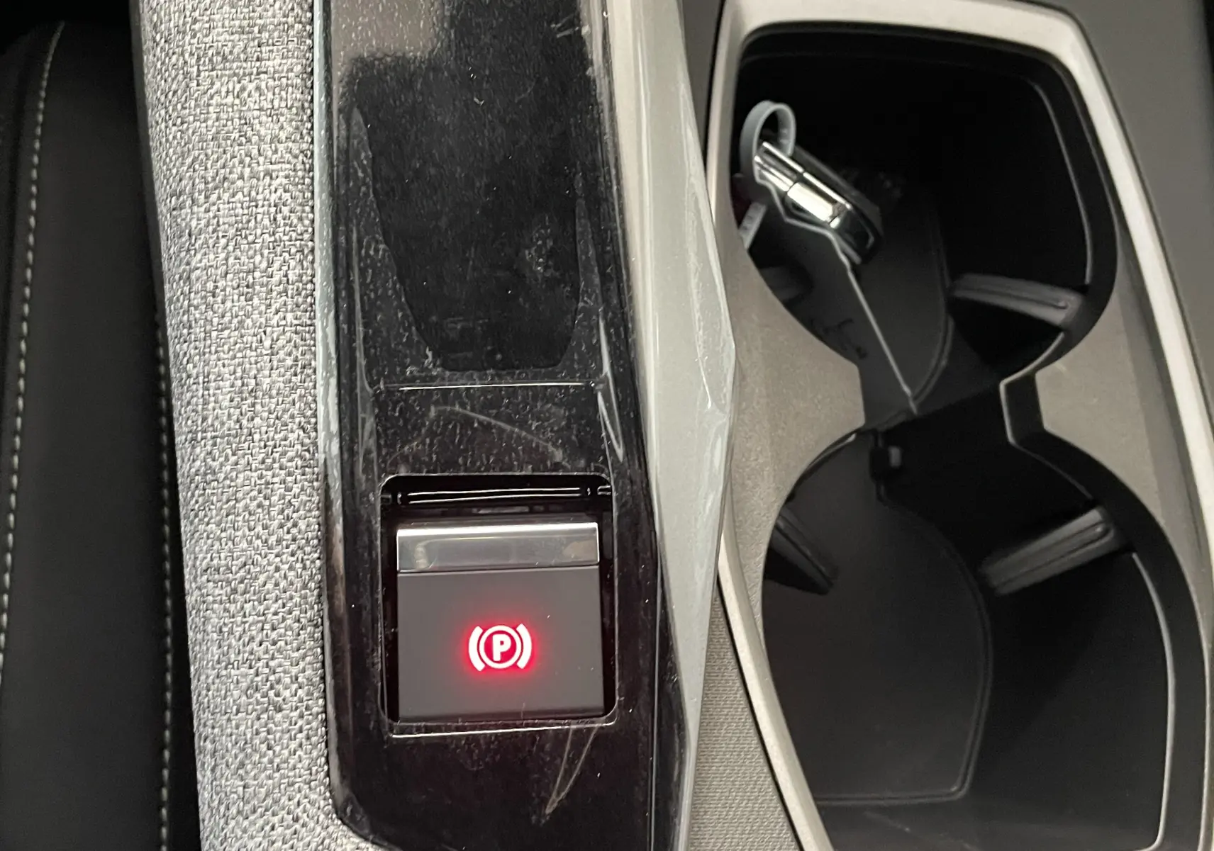 Gros plan sur la console centrale du Peugeot 3008 blanc, avec bouton de frein à main électronique allumé et porte-gobelets noirs.