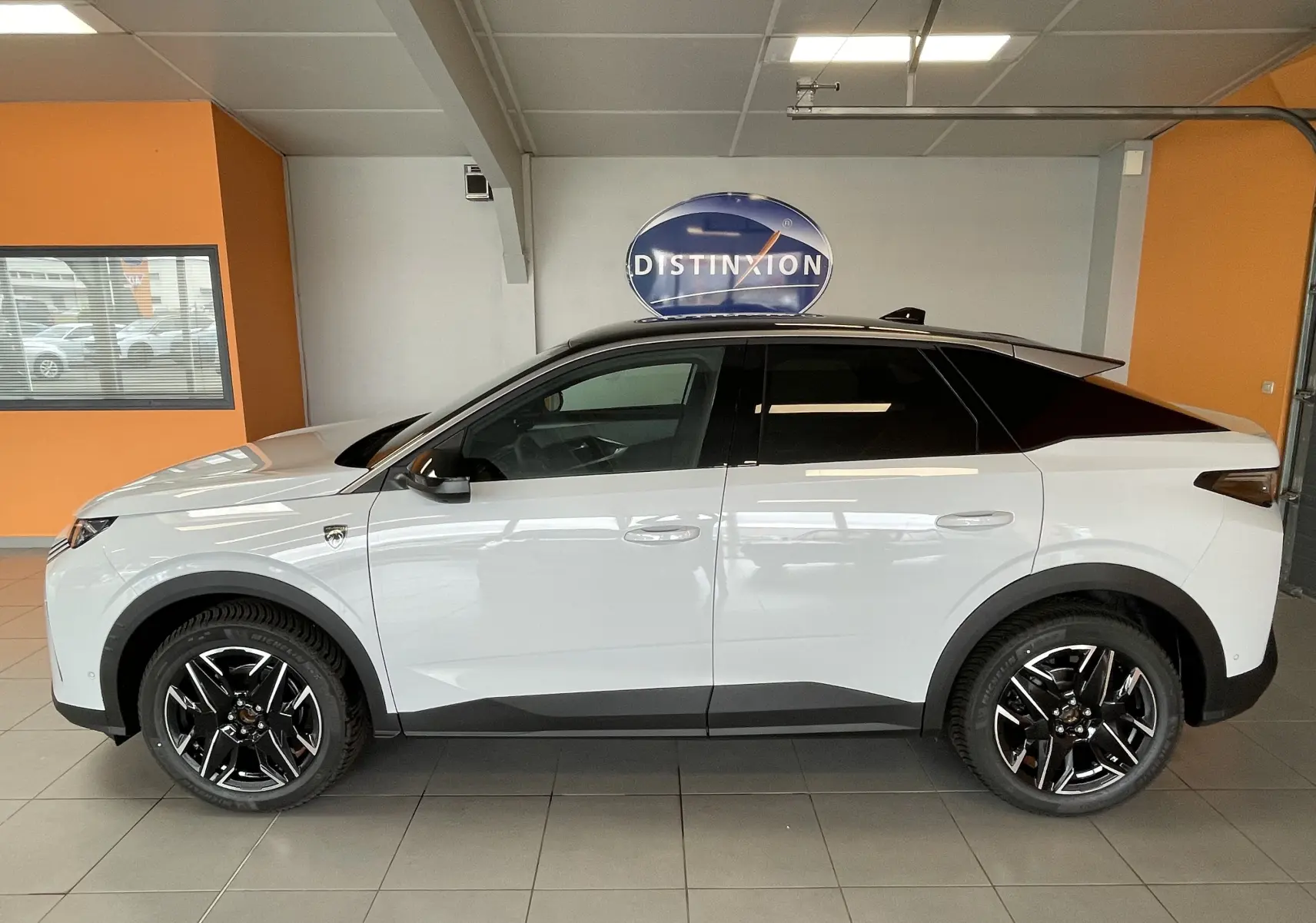 Vue de profil côté gauche d’un Peugeot 3008 Hybrid blanc Okenite avec toit noir et jantes alliage noires en showroom.