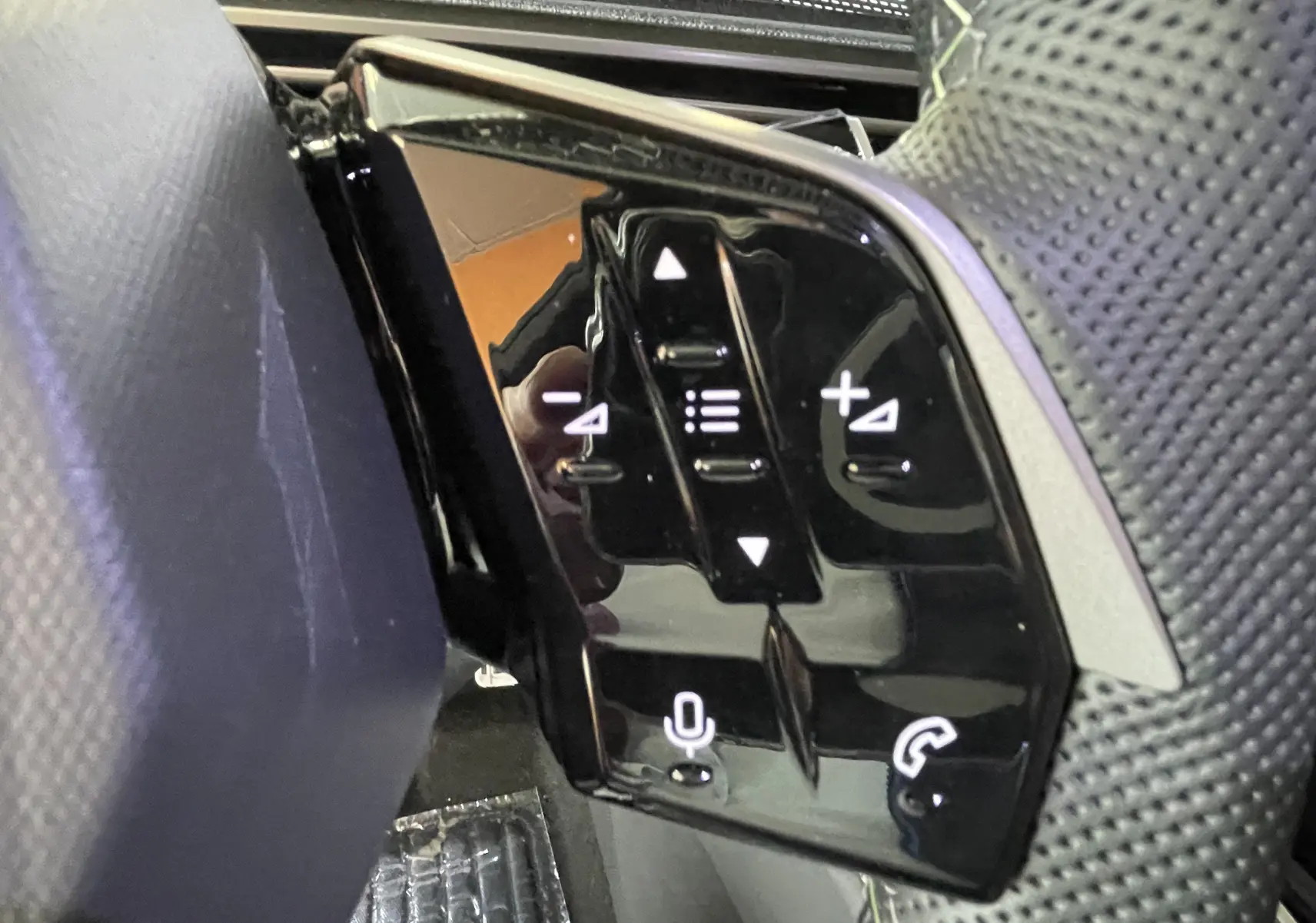 Gros plan sur les commandes tactiles noires du volant côté gauche du Peugeot 3008 Hybrid blanc Okenite.