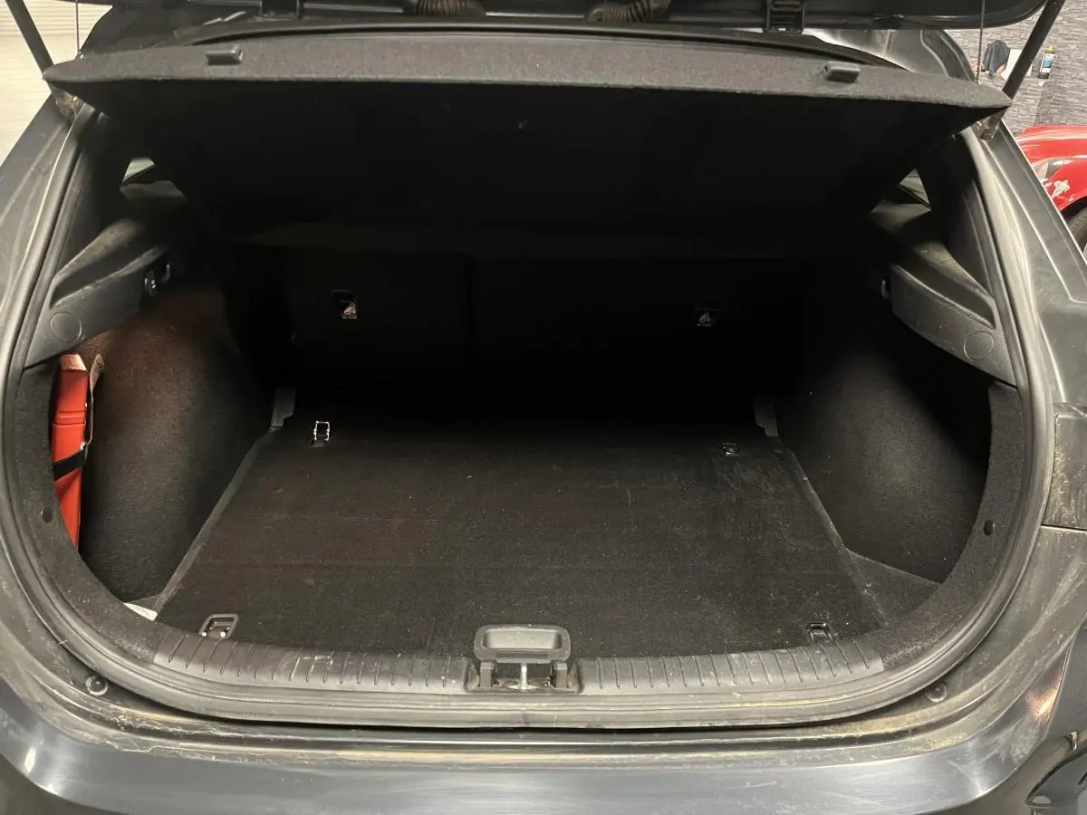 Coffre ouvert vu de l'arrière d'une Kia Ceed gris, montrant l'espace de chargement vide et les finitions intérieures.