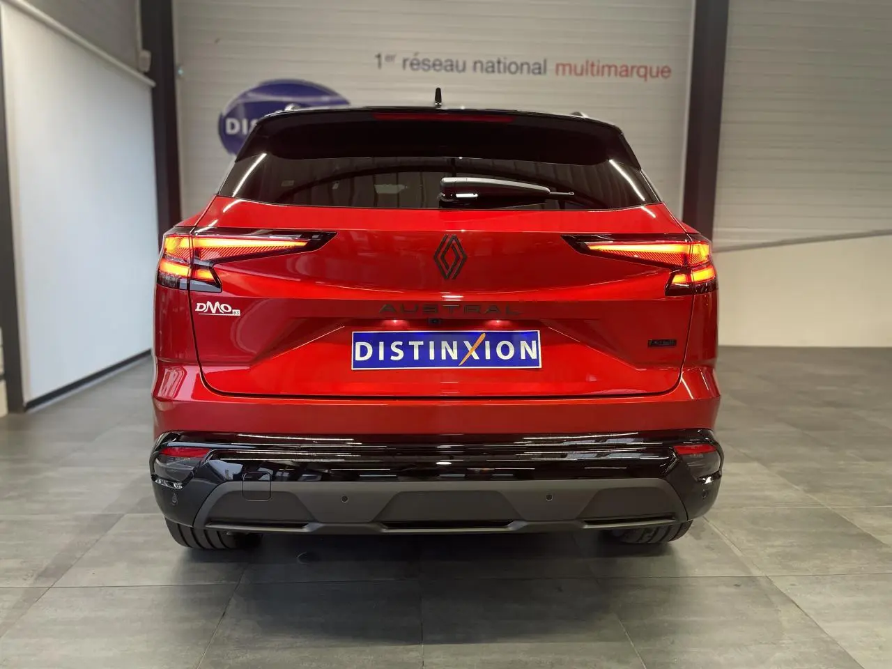 Vue arrière du Renault Austral rouge métallisé avec toit noir, feux LED allumés et logo noir brillant distinctif.