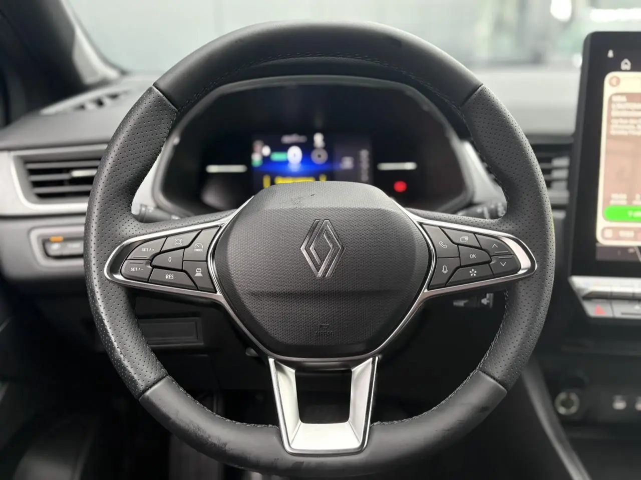 Vue rapprochée du volant en cuir noir perforé du Renault Captur 2025 avec commandes intégrées et tableau de bord numérique flou.