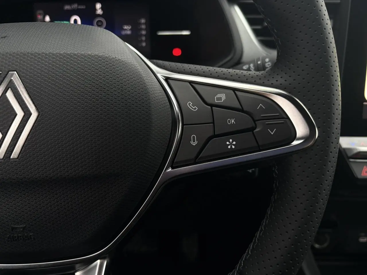 Gros plan sur le volant noir perforé du Renault Captur 2025, avec commandes multifonctions et logo Renault central argenté.