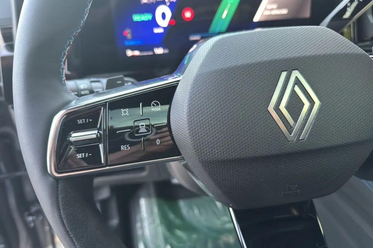 Gros plan sur le volant cuir multifonctions noir avec logo Renault, tableau de bord digital en arrière-plan flou.
