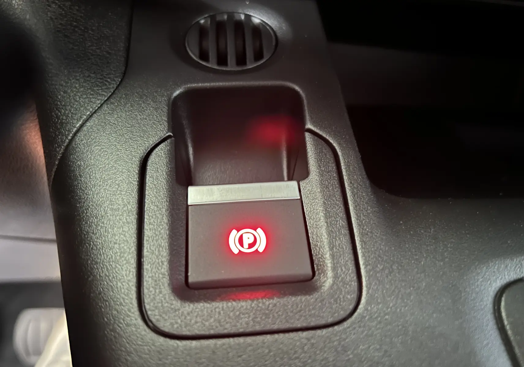 Gros plan sur le bouton de frein à main électrique rouge dans l'habitacle du Citroën Berlingo Multispace gris acier.