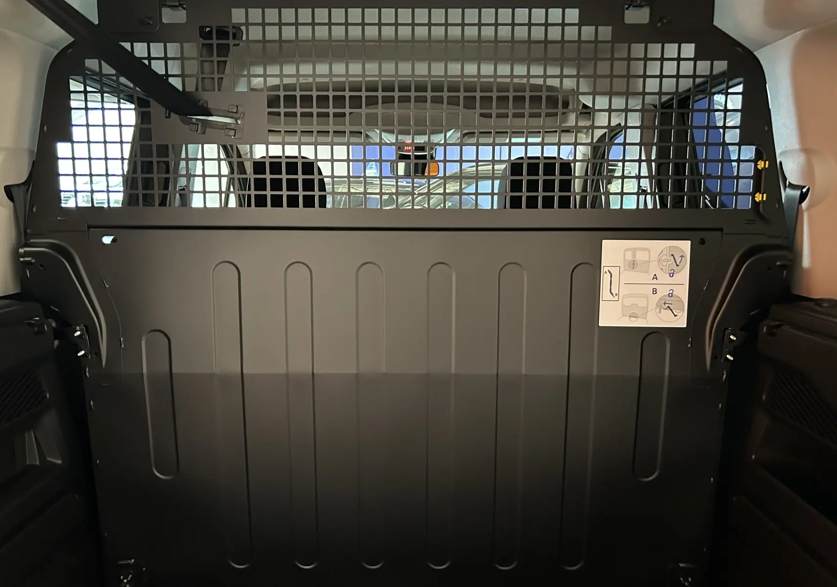 Vue intérieure arrière du Citroën Berlingo Multispace gris acier avec cloison de séparation métallique et grille de sécurité.