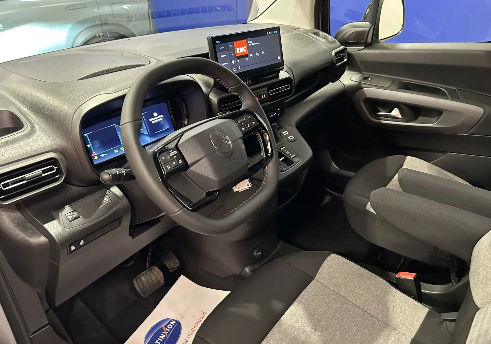 Vue intérieure côté conducteur du Citroën Berlingo Multispace 2026, volant cuir, tableau de bord digital et sièges tissu gris et noir.