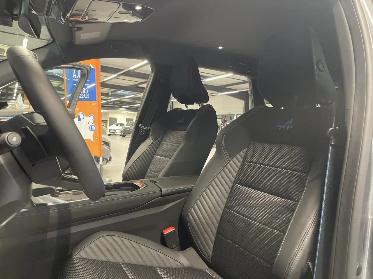 Vue intérieure côté conducteur du Renault Austral 2025 avec sièges noirs en cuir et logo Alpine brodé sur les appuie-têtes.