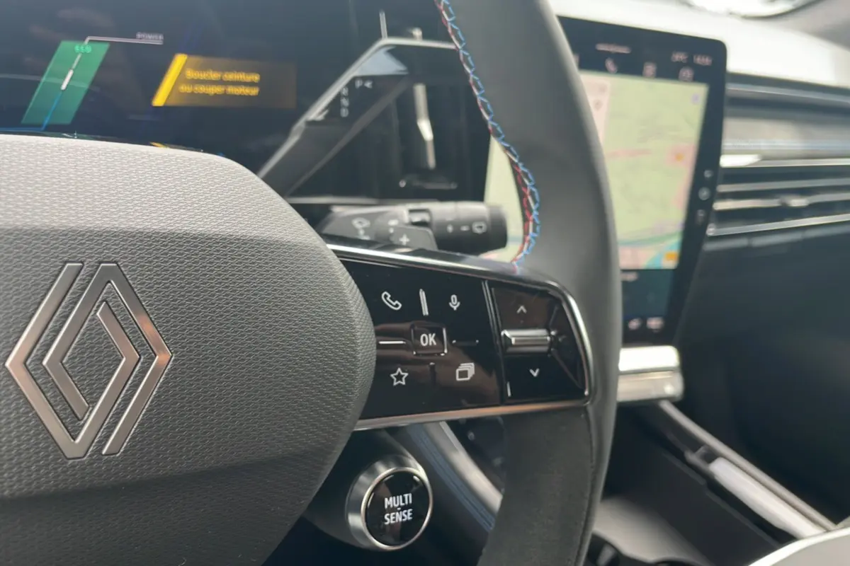 Gros plan sur le volant multifonctions avec surpiqûres bleues et écran tactile du tableau de bord du Renault Austral gris schiste.