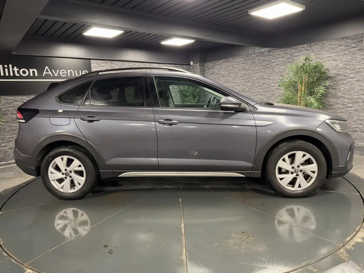 Profil droit d'un Volkswagen Taigo gris 2024 avec jantes alliage Belmopan et lignes fluides sous un éclairage intérieur.