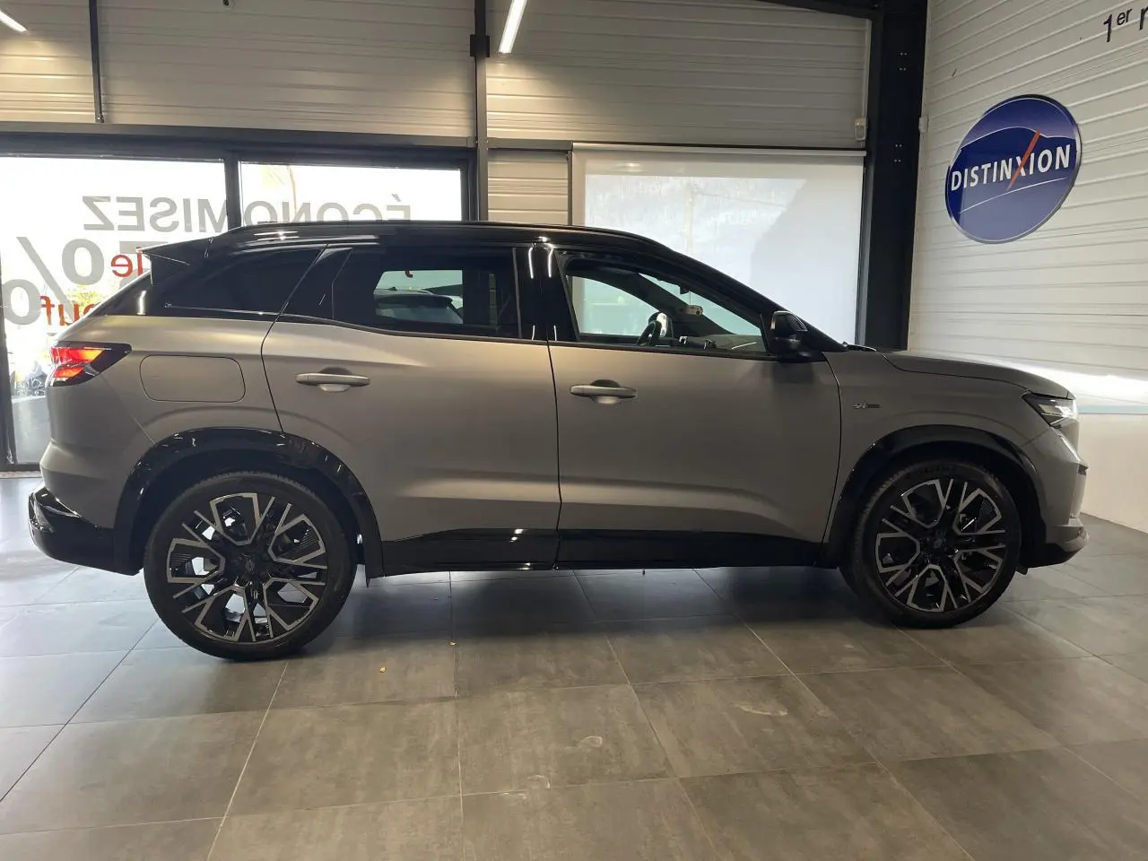 Profil côté gauche du Renault Austral gris satin mat avec toit noir et jantes alliage noires en showroom.