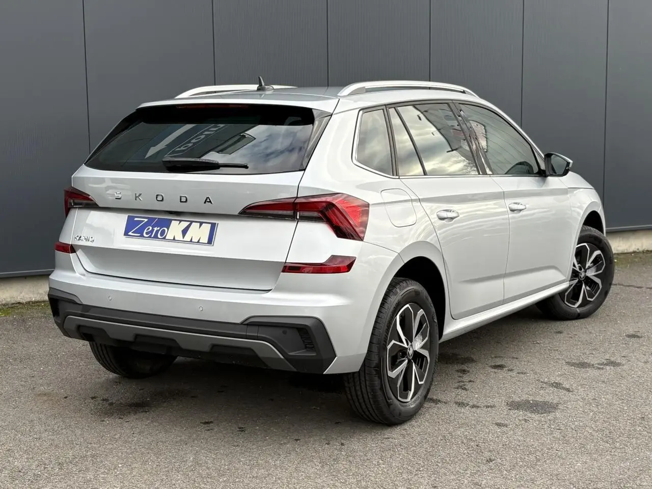 Vue 3/4 arrière droite d'un Skoda Kamiq gris argent avec vitres surteintées et jantes alliage noires.