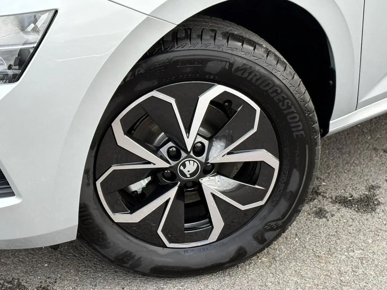 Gros plan sur la roue avant droite d’une Skoda Kamiq gris argent avec jante alliage noire et argentée au design géométrique.