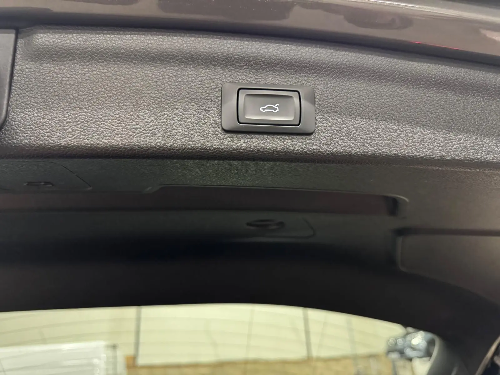 Bouton d'ouverture électrique du coffre sur la garniture intérieure noire d'un Audi Q3 Business gris.