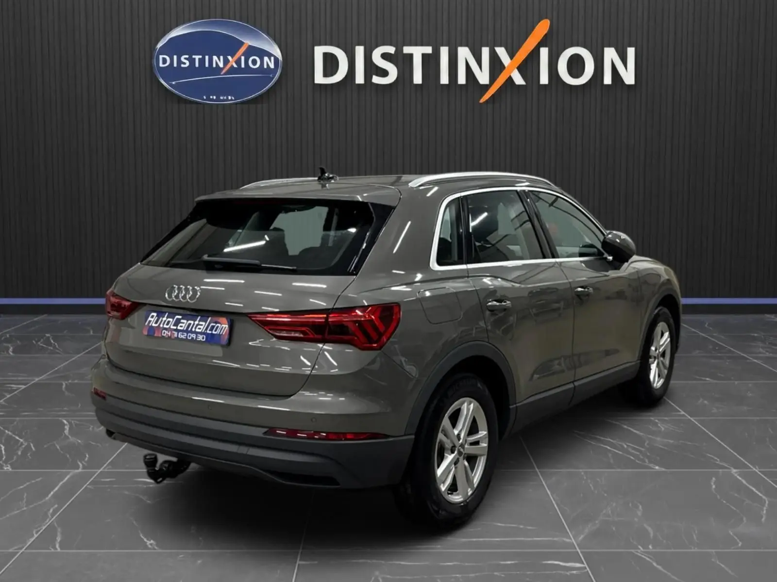 Vue 3/4 arrière droite d'un Audi Q3 Business gris avec feux arrière LED dynamiques et attelage visible en intérieur showroom.