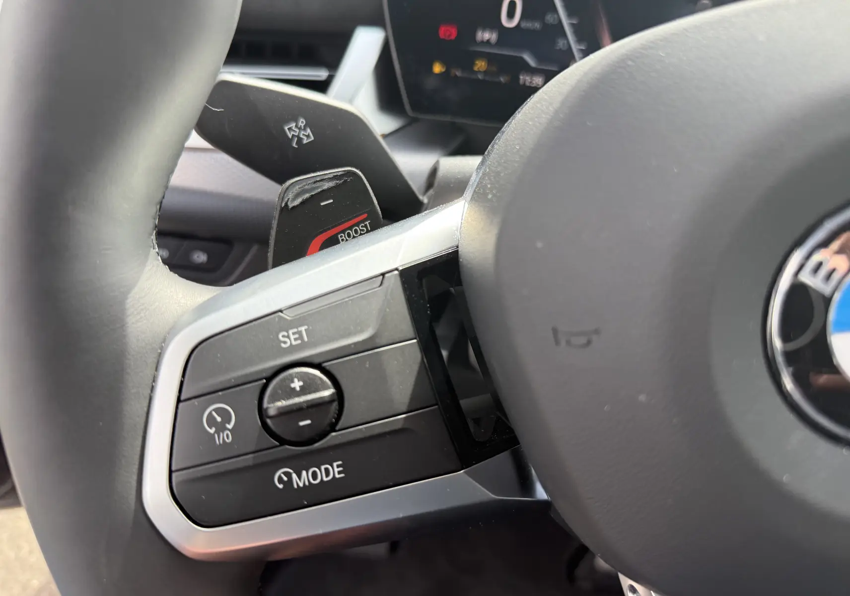Gros plan sur les commandes au volant côté gauche d’un BMW X2 2025, avec bouton boost et finition cuir noire.