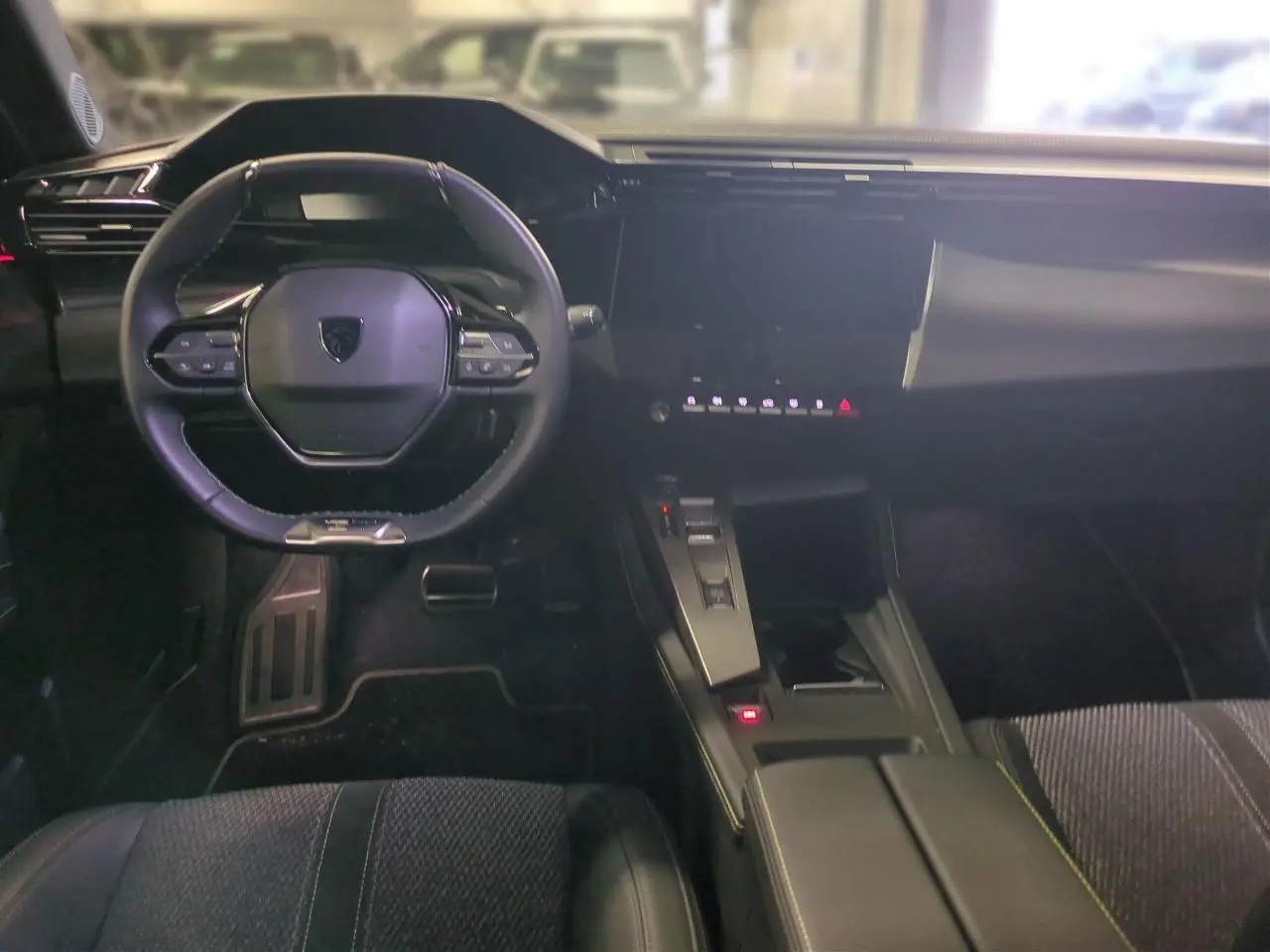Intérieur noir de la Peugeot 308 2025, vue frontale du poste de conduite avec volant cuir et écran tactile central.