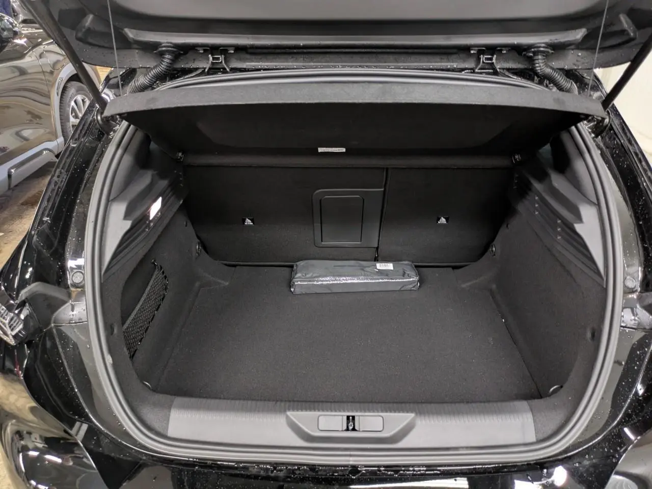 Coffre ouvert vu de l'arrière d'une Peugeot 308 noir Perla, avec un espace de chargement propre et un kit de sécurité posé.
