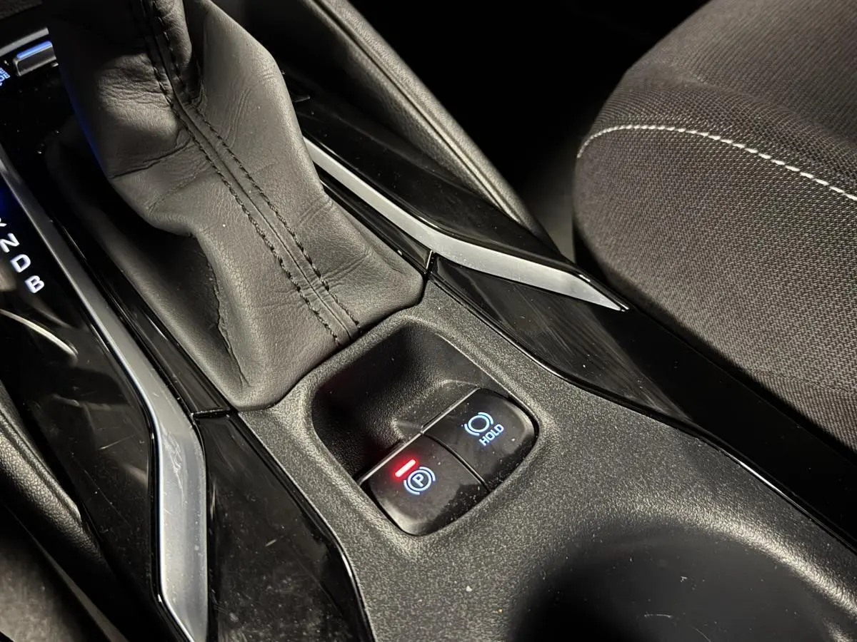 Gros plan sur la console centrale noire laquée de la Toyota Corolla hybride 2022 avec levier de vitesses cuir et frein électrique.