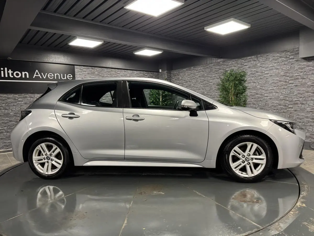 Profil côté gauche d'une Toyota Corolla hybride gris métallisé avec jantes alliage 16 pouces dans un showroom.