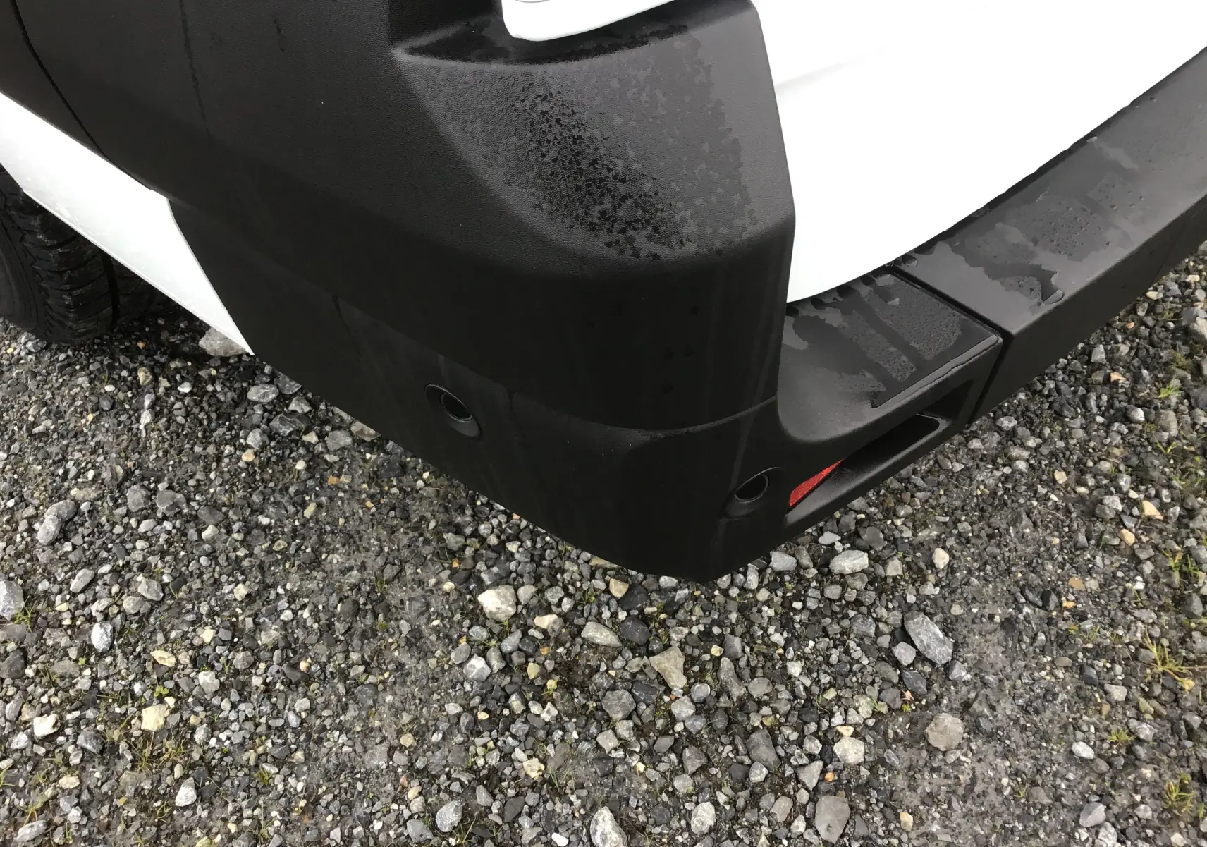 Gros plan sur l'angle arrière droit du pare-chocs noir d'un Renault Master blanc, avec capteurs de recul visibles.