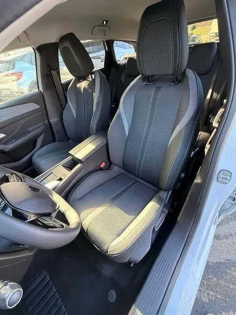 Vue intérieure côté conducteur de la Peugeot 308 Hybrid 145 e-DCS6 Allure 2025 blanche, sièges tissu gris avec surpiqûres.