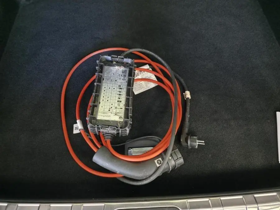 Câble de recharge orange et noir posé dans le coffre d'une Peugeot 408 gris métallisé, vue plongeante.