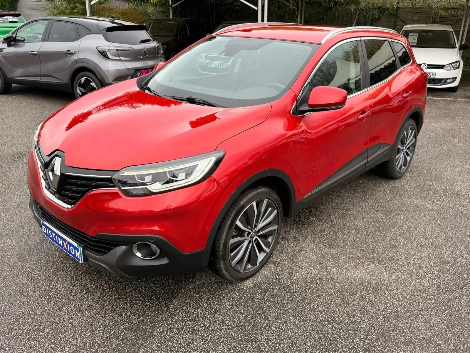 Vue 3/4 avant droit d’un Renault Kadjar rouge flamme avec jantes alliage bicolores et calandre noire distinctive.