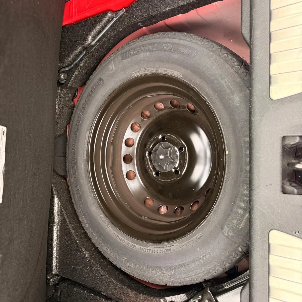 Vue rapprochée de la roue de secours noire dans le coffre d’un Renault Kadjar rouge flamme de 2016.