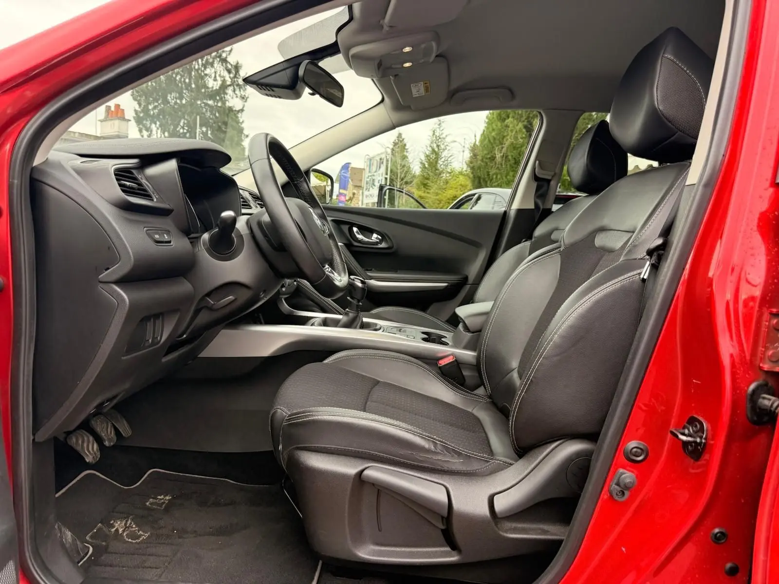 Intérieur côté conducteur du Renault Kadjar rouge flamme 2016, sièges cuir noir et tableau de bord moderne.