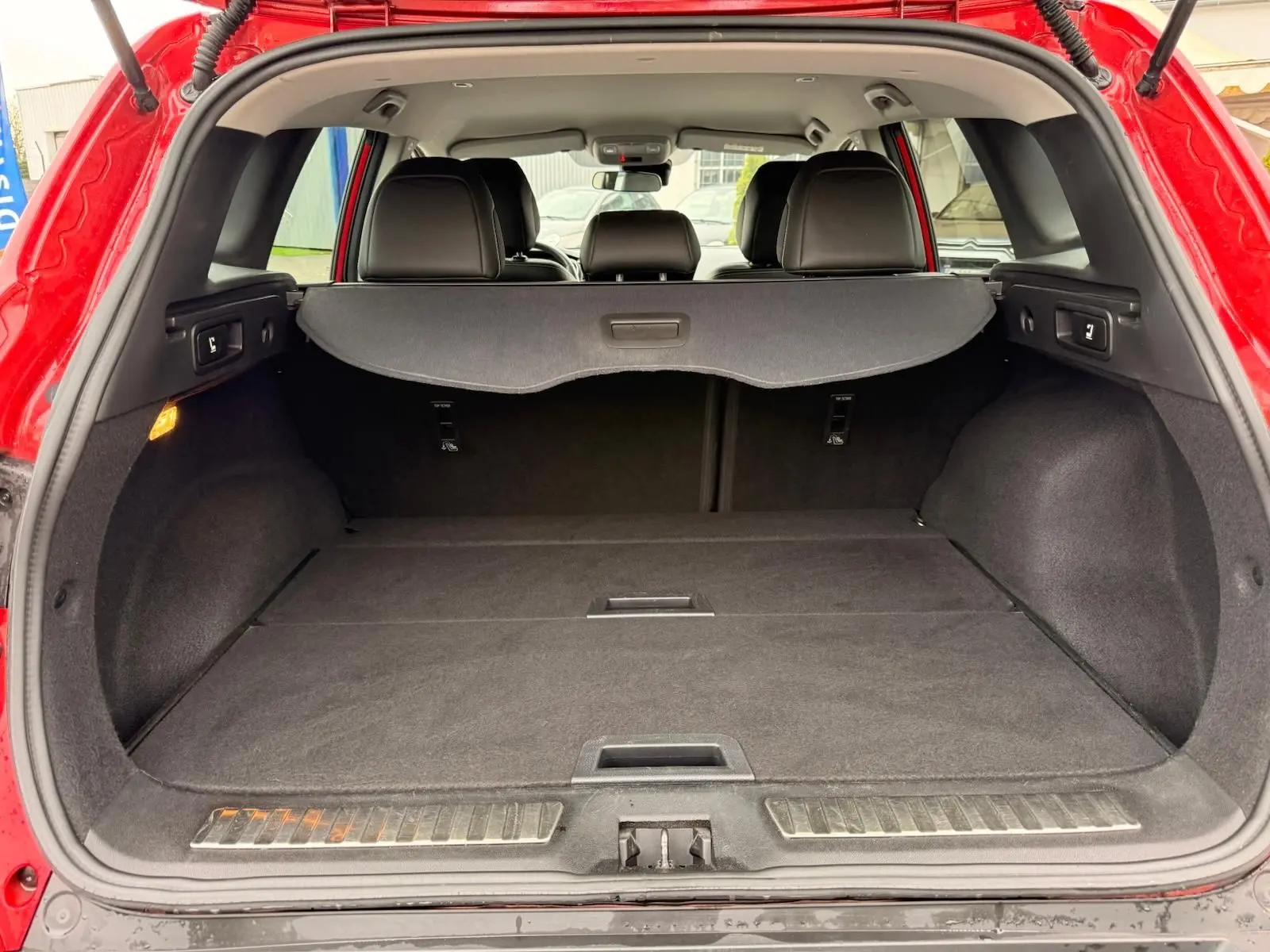 Vue arrière ouverte du coffre spacieux du Renault Kadjar rouge flamme, avec cache-bagages et sièges noirs visibles.