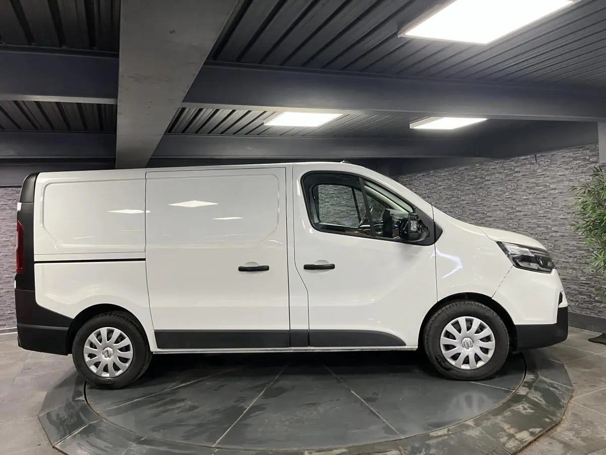 Vue de profil côté droit d'un utilitaire Nissan Primastar blanc avec enjoliveurs de roues et protections noires.