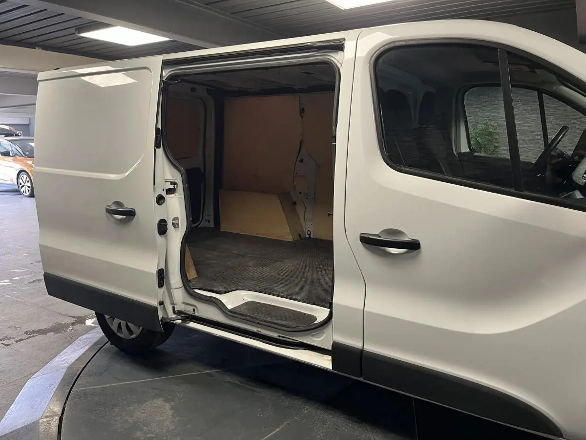 Vue latérale droite d'un Nissan Primastar blanc avec porte coulissante ouverte montrant l'espace de chargement bois.