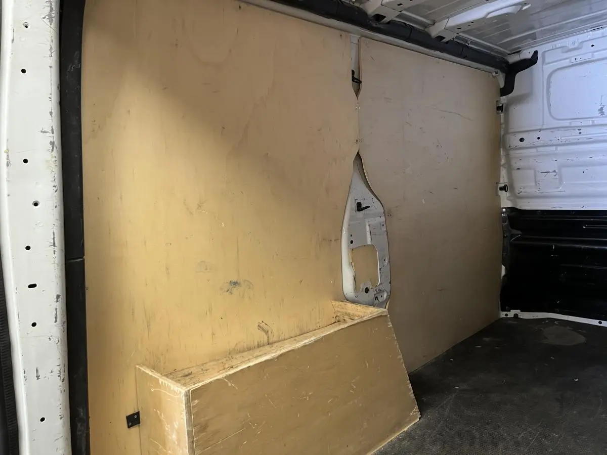 Vue intérieure du compartiment de chargement d'un utilitaire Nissan Primastar blanc avec plancher et protections latérales en bois.