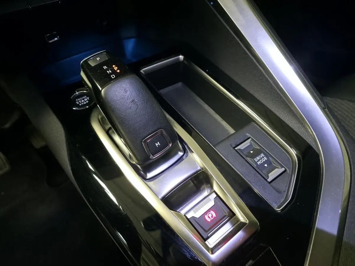 Gros plan sur la console centrale noire du Peugeot 5008 gris, avec levier de boîte auto et bouton Drive Mode.