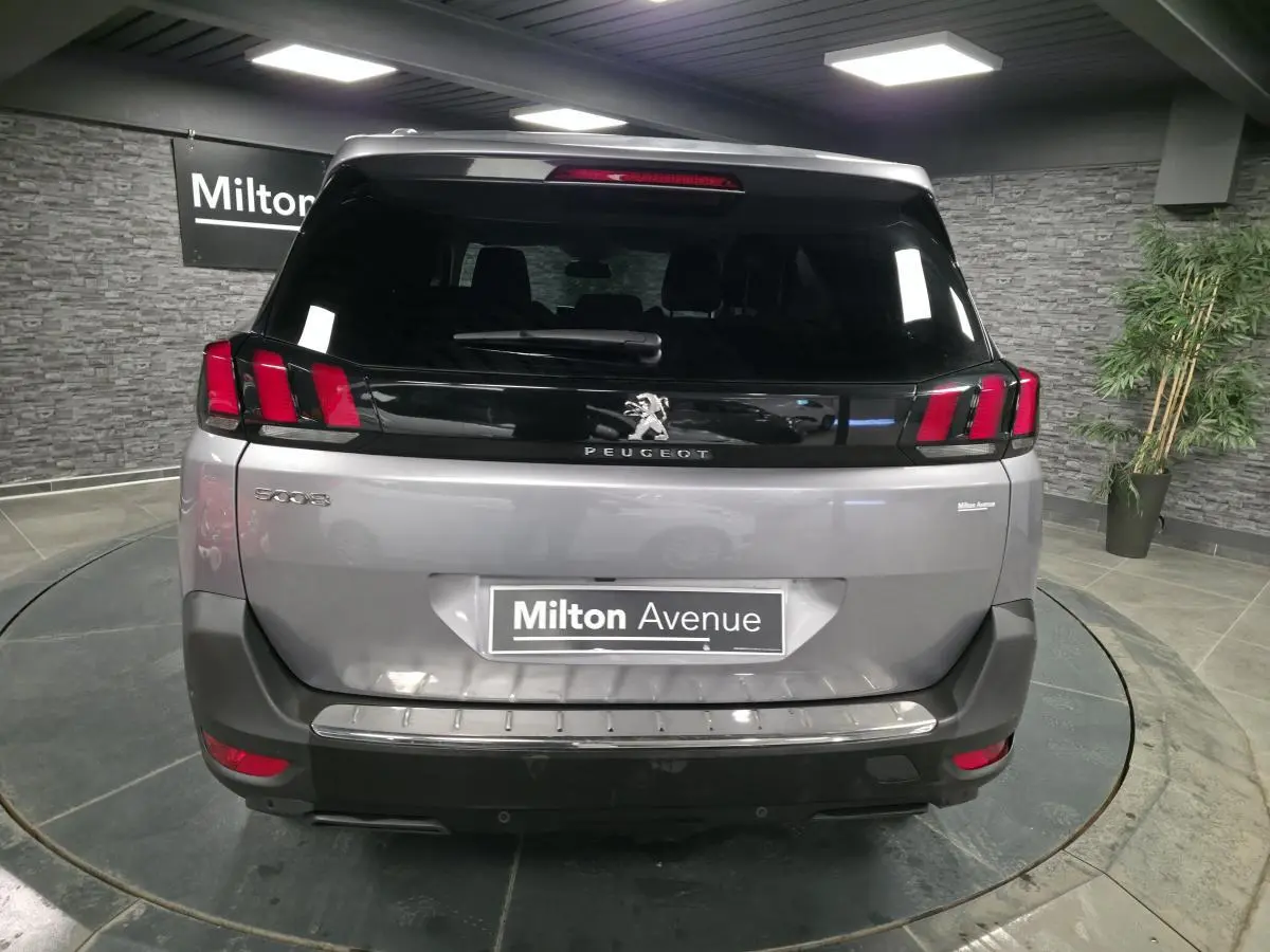 Vue arrière d'un Peugeot 5008 gris métallisé avec feux arrière à griffes rouges et lunette teintée noire.