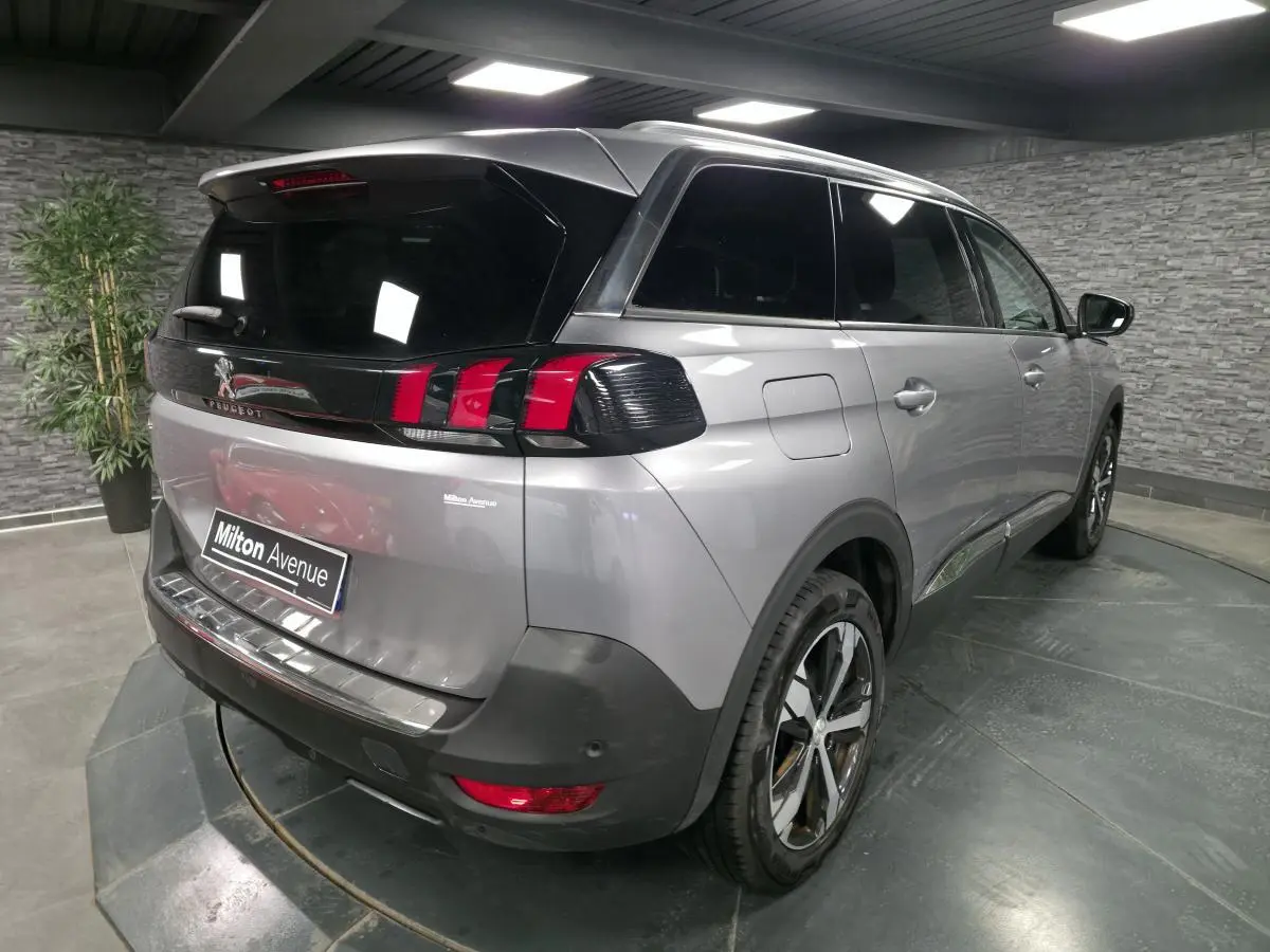 Vue 3/4 arrière droite d'un Peugeot 5008 gris métallisé avec vitres surteintées et jantes alliage bi-ton.