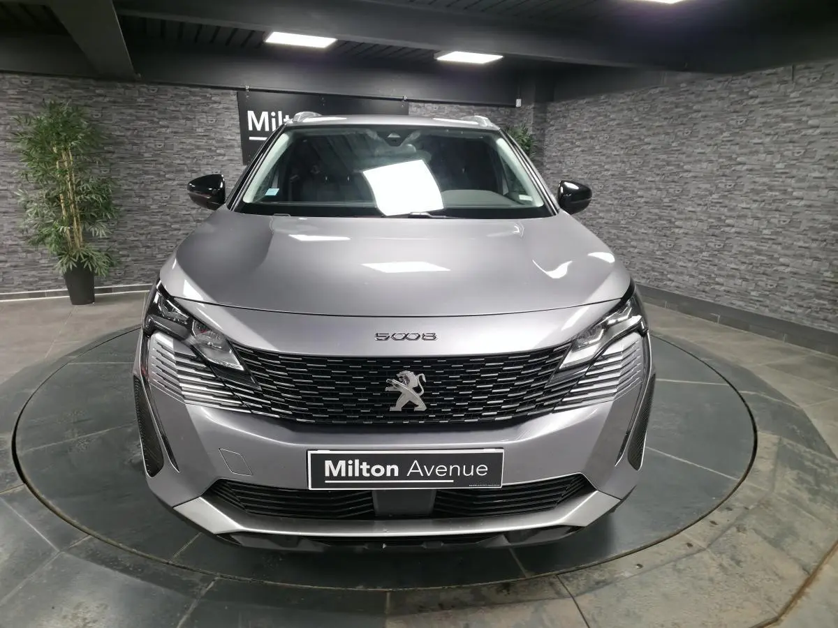 Vue frontale d'un Peugeot 5008 gris métallisé avec calandre à damier chromé et barres de toit visibles.