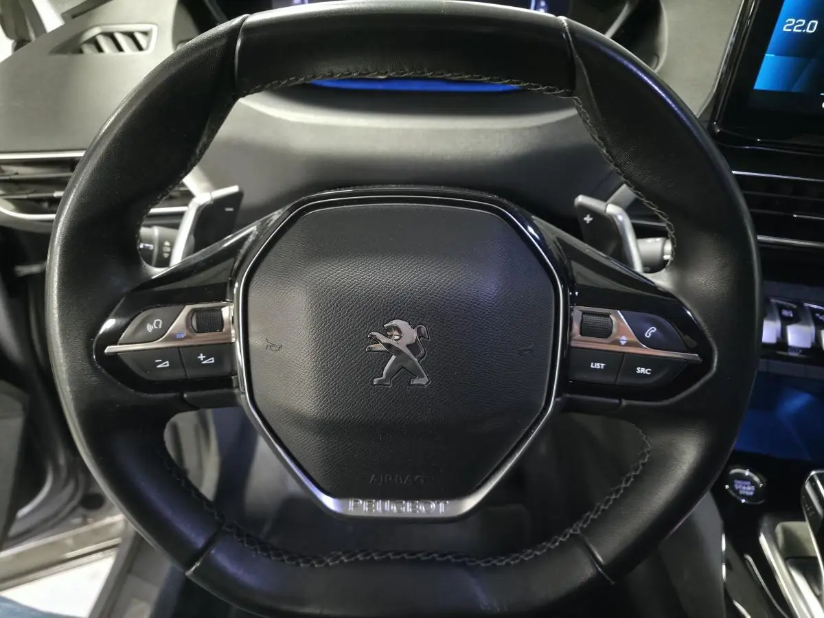 Gros plan sur le volant cuir noir du Peugeot 5008 2022 avec commandes intégrées et logo lion central.