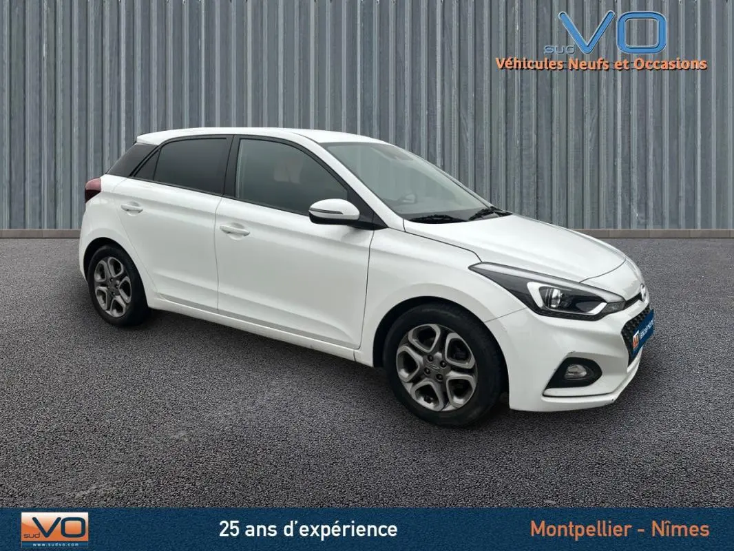 Hyundai i20 blanc vue 3/4 avant droit, jantes alliage 16 pouces et phares antibrouillard visibles