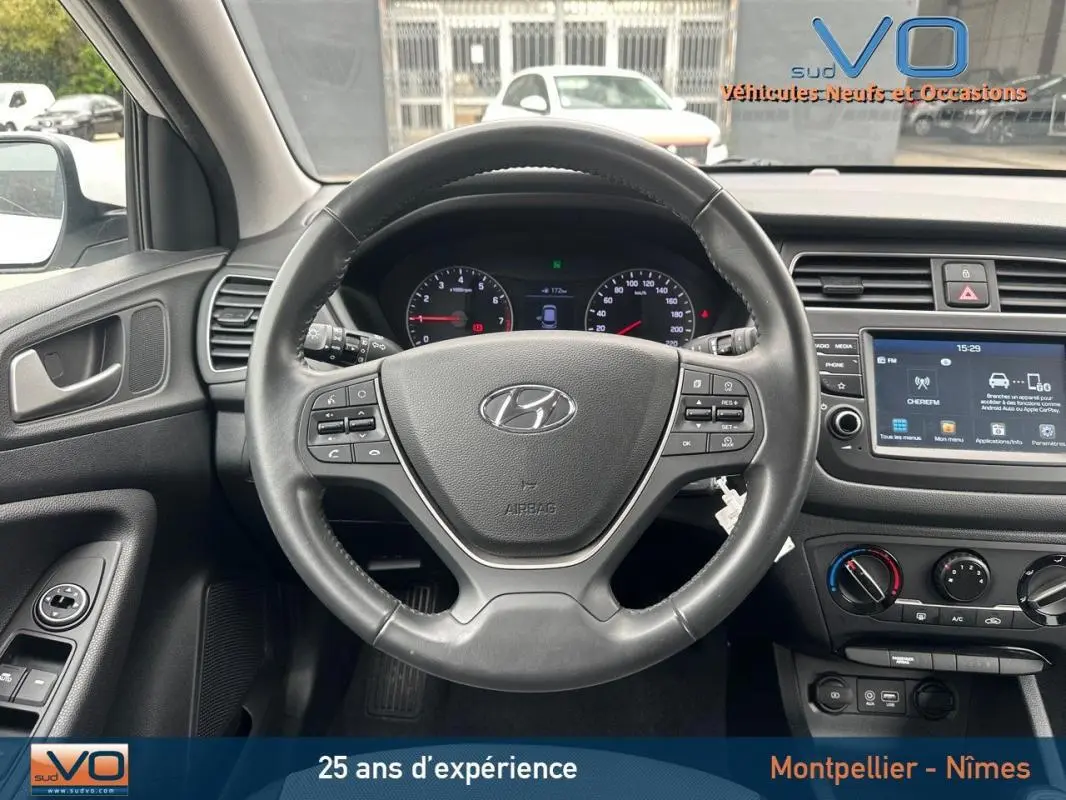 Vue intérieure centrée sur le volant noir de la Hyundai i20 blanche 2019 avec tableau de bord et écran tactile visible.