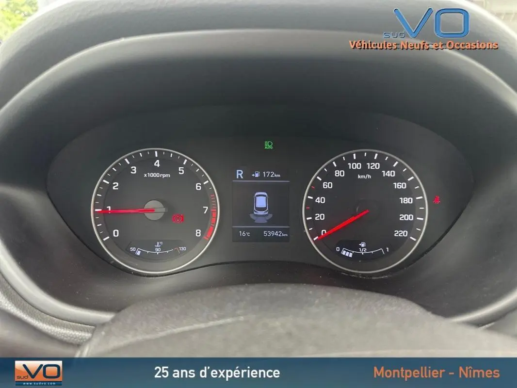 Gros plan sur le tableau de bord numérique de la Hyundai i20 blanche, affichant compte-tours et vitesse, avec écran central actif.