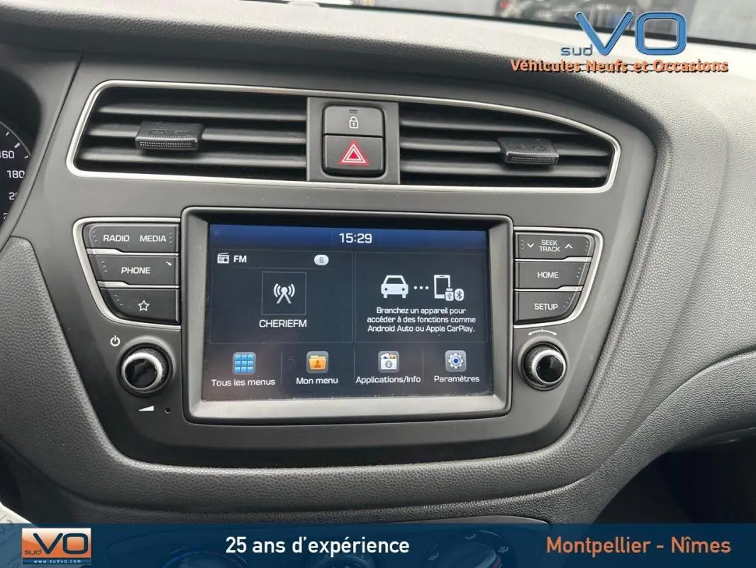 Vue rapprochée du tableau de bord de la Hyundai i20 blanche 2019, mettant en valeur l'écran tactile multimédia et les commandes environnantes.