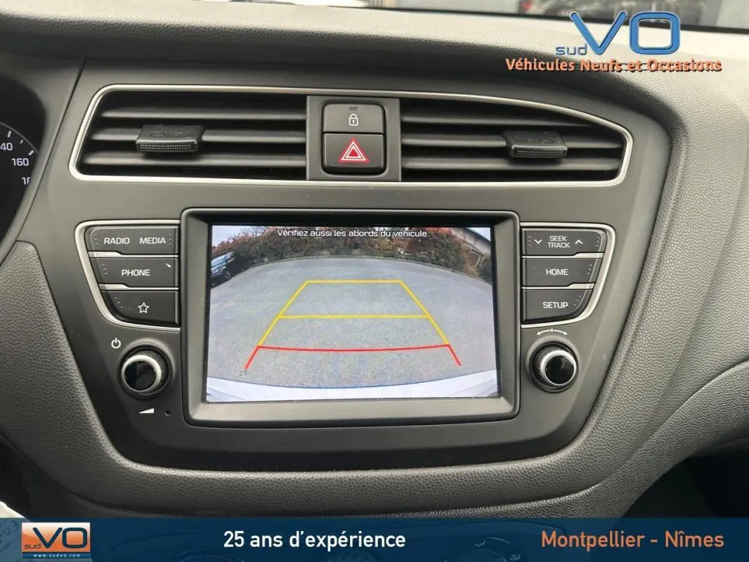 Écran central de la Hyundai i20 blanc 2019 montrant la caméra de recul avec guidage coloré, tableau de bord noir.