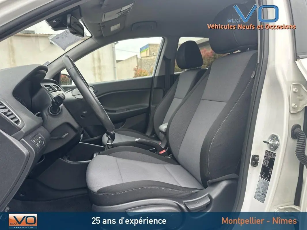 Vue intérieure côté conducteur de la Hyundai i20 blanche 2019, sièges tissu gris et volant réglable visible.