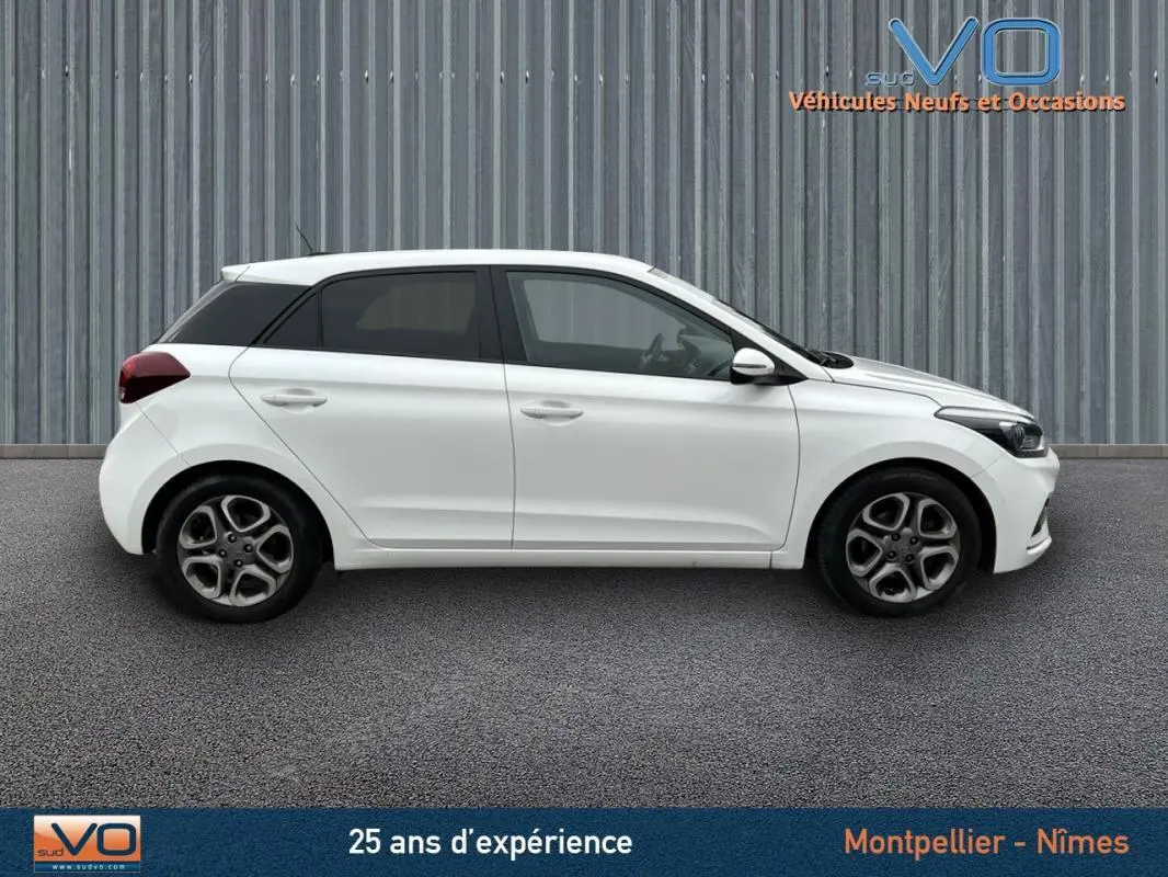 Profil côté gauche de la Hyundai i20 blanche 2019 avec jantes alliage 16 pouces sur fond industriel.