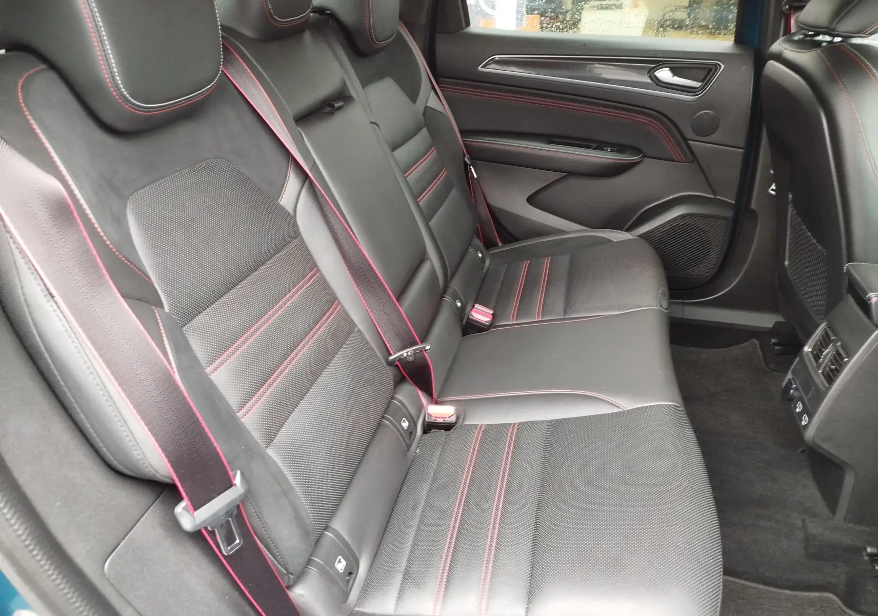 Vue intérieure arrière côté droit montrant les sièges noirs en cuir et alcantara avec surpiqûres rouges du Renault Arkana.