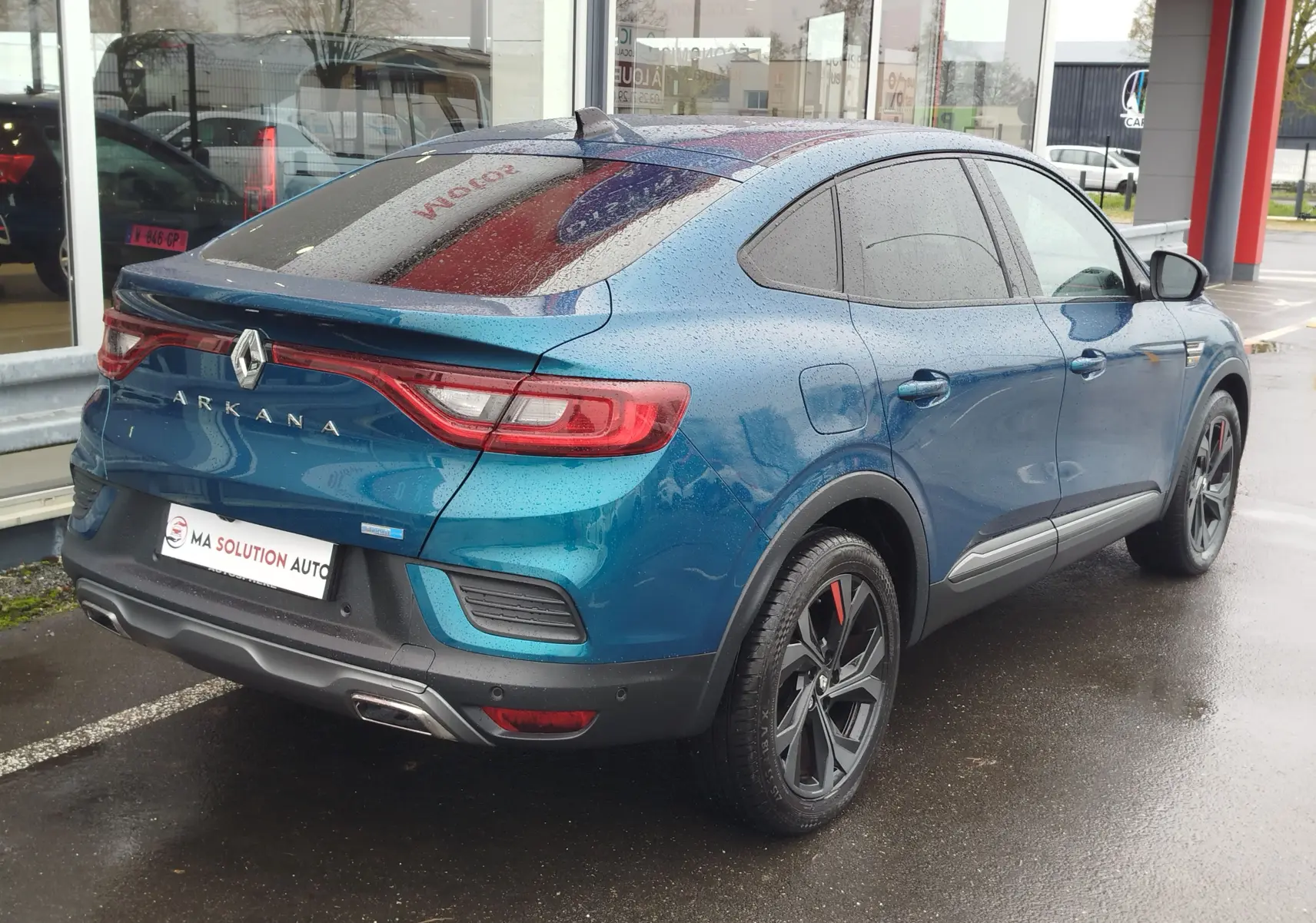 Vue 3/4 arrière droite d’un Renault Arkana bleu Zanzibar 2022 avec jantes noires et feux arrière LED distinctifs.