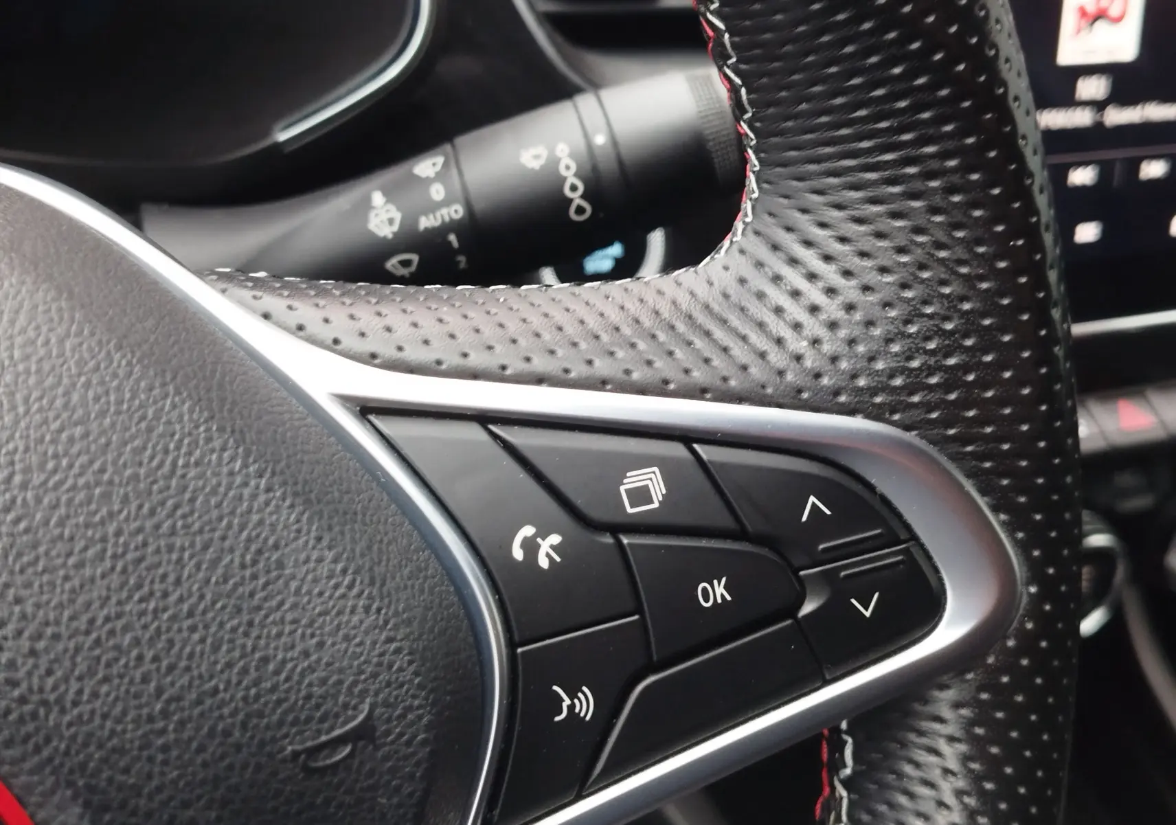 Gros plan sur les commandes noires du volant perforé avec surpiqûres rouges du Renault Arkana bleu Zanzibar, version RS Line 2022.